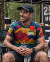 Man wearing a vrt rising peaks running shirt with 'VRT' logo, sitting outdoors at an event.